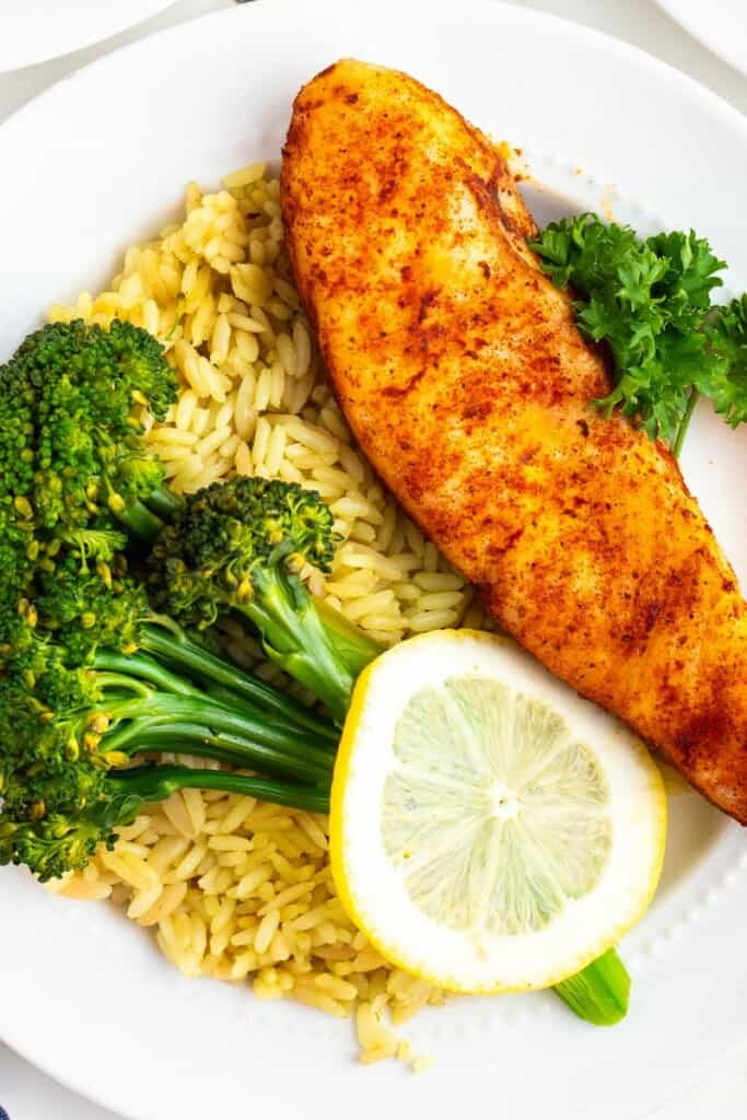 A close up view of plated seasoned halibut with rice and broccoli.