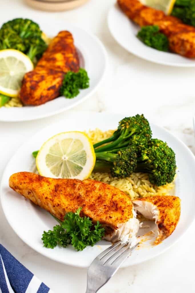 Three plates of seasoned halibut with rice and broccoli. A fork lifting one bite from the front plate.