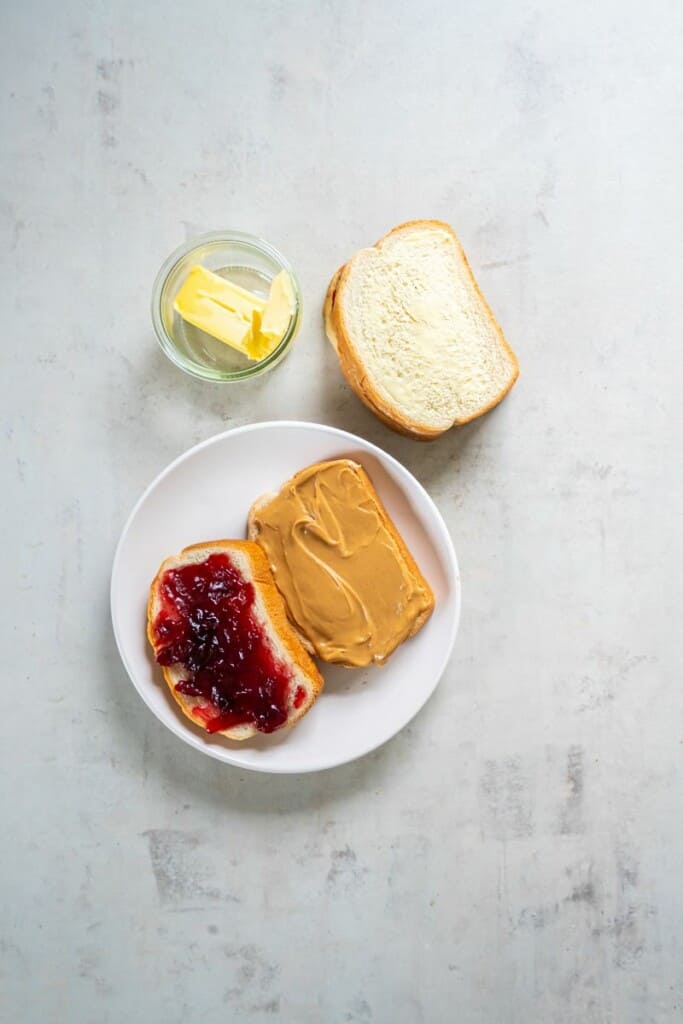 One slice of bread with peanut butter, another slice of bread with jelly, resting on a white plate.