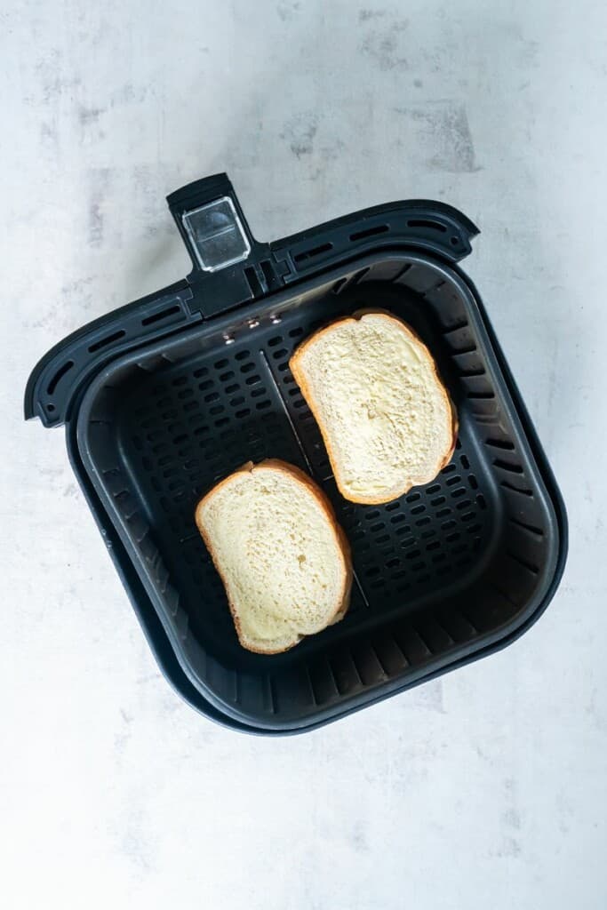 Two peanut butter and jelly sandwiches resting in a black air fryer basket.
