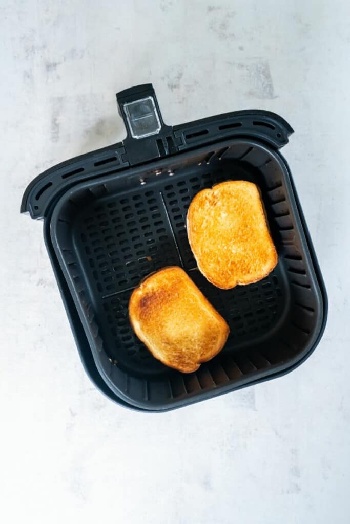 Two toasted peanut butter and jelly sandwiches resting in a black air fryer basket.