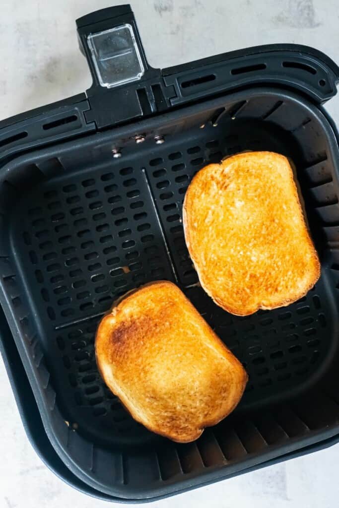 Closeup view of two peanut butter and jelly sandwiches in a black air fryer basket.