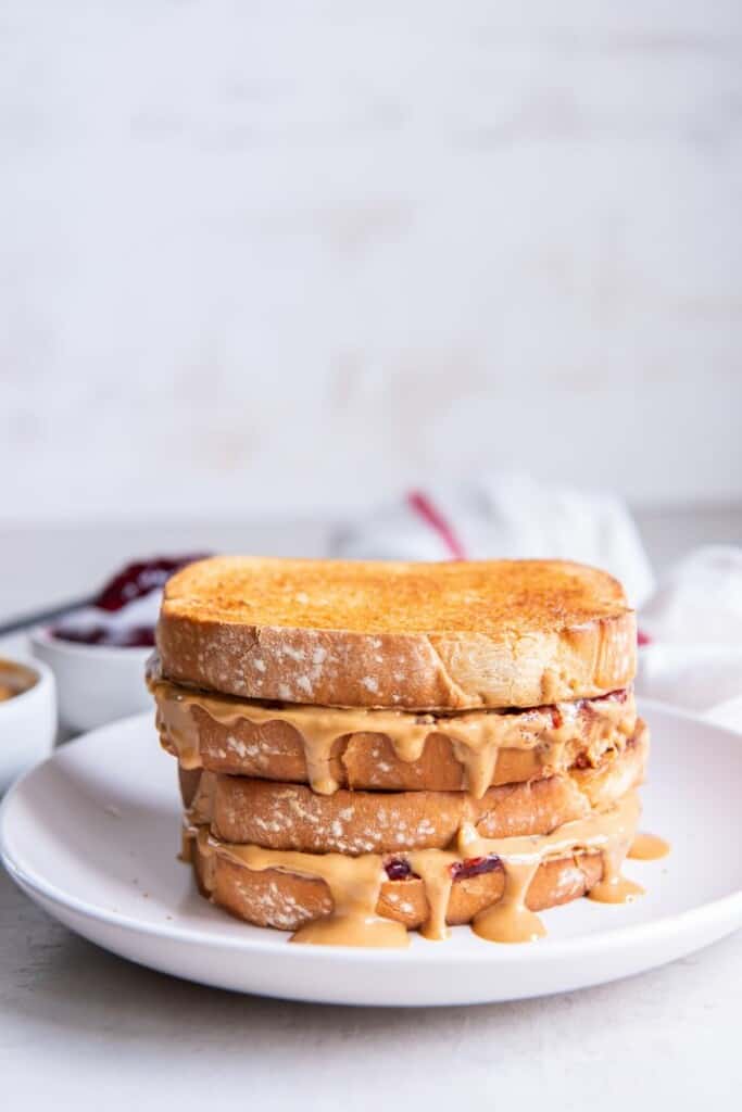 Two peanut butter and jelly sandwiches stacked on a white plate.