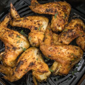 Seasoned chicken wings in a black air fryer basket after cooking.