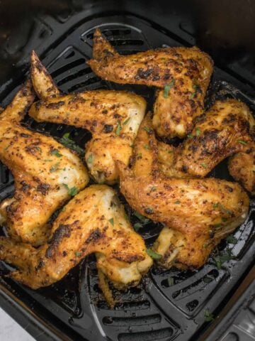 Seasoned chicken wings in a black air fryer basket after cooking.