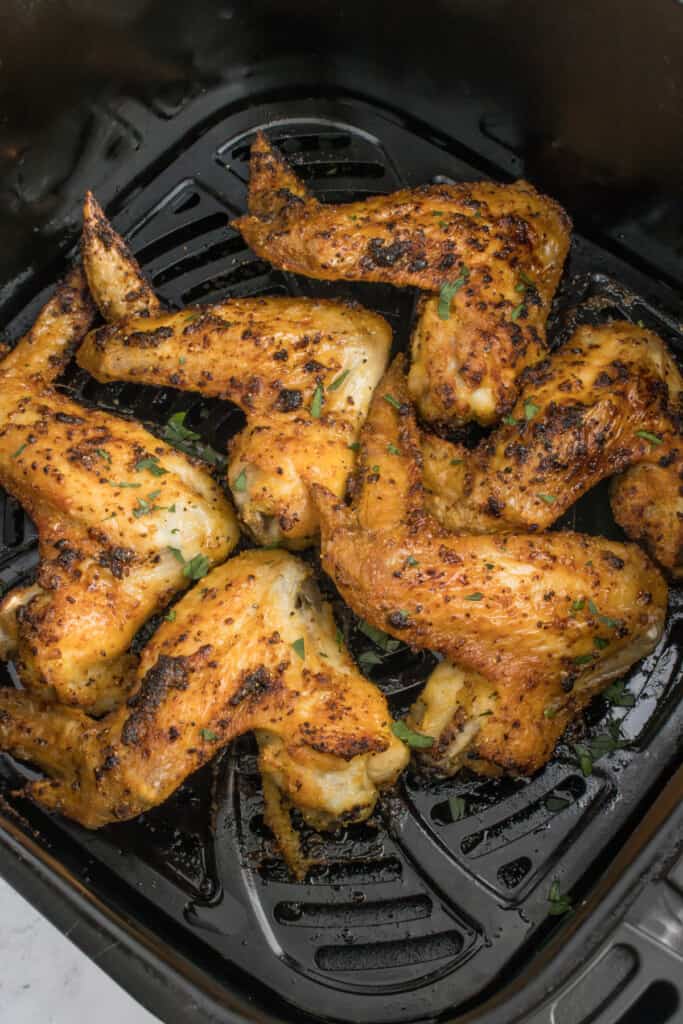 Seasoned chicken wings in a black air fryer basket after cooking.