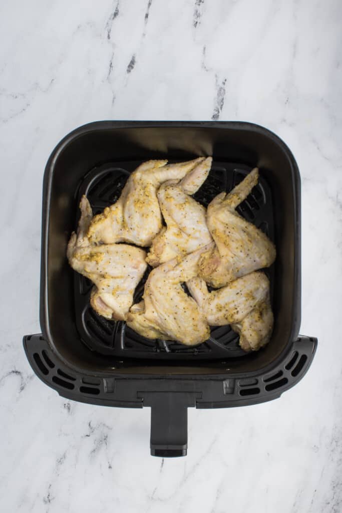 Seasoned chicken wings in a single layer of a black air fryer basket.