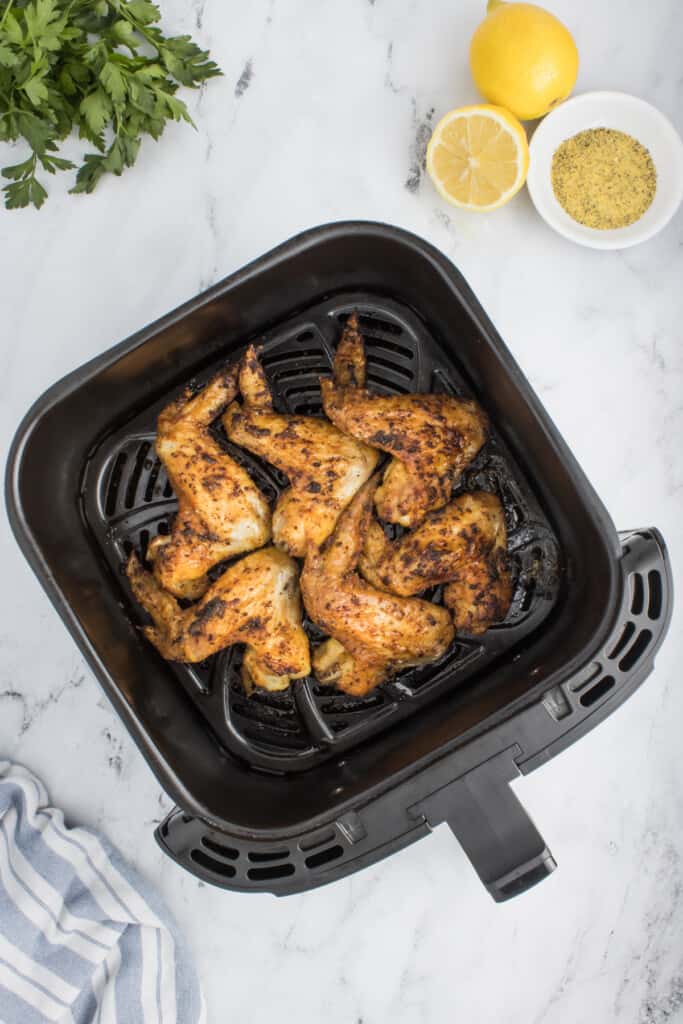 Seasoned chicken wings in a black air fryer basket halfway through cooking.