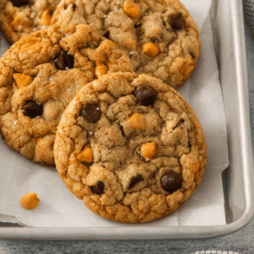 Four butterscotch chocolate chip cookies on a parchment lined baking sheet.