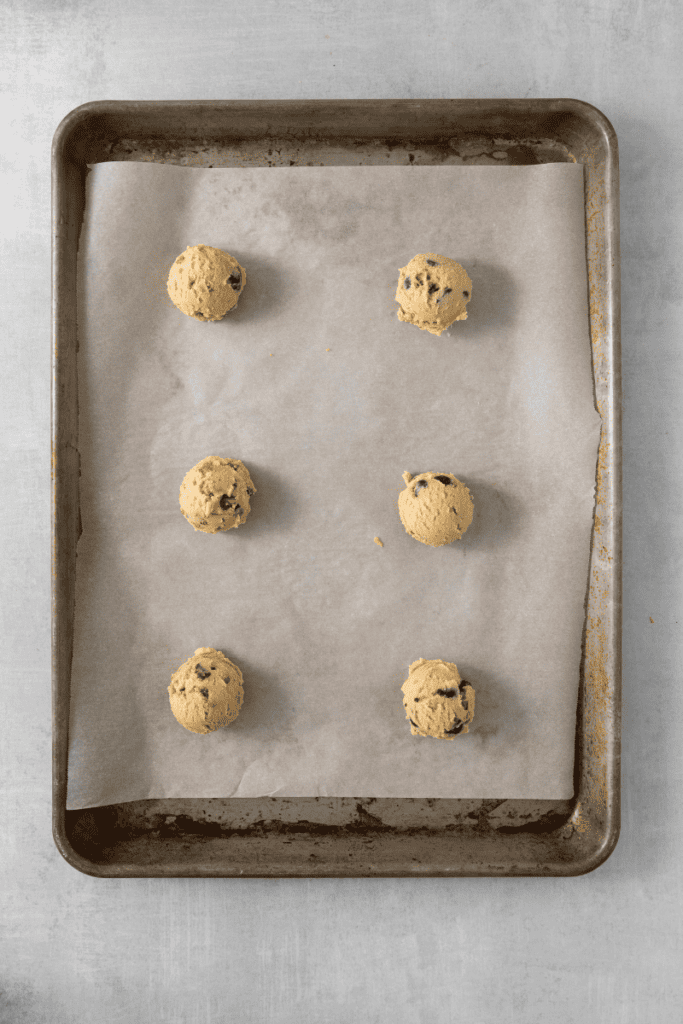 Six cookie dough balls on a parchment lined baking sheet.