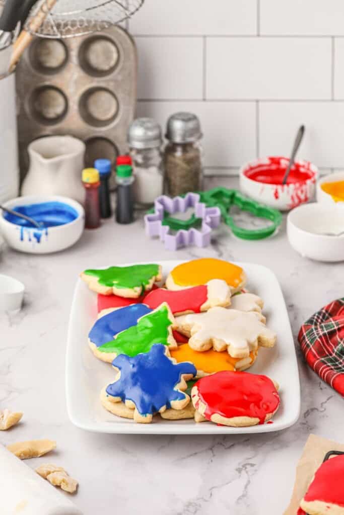 Decorated Christmas sugar cookies on a serving platter with decorating supplies in the background.