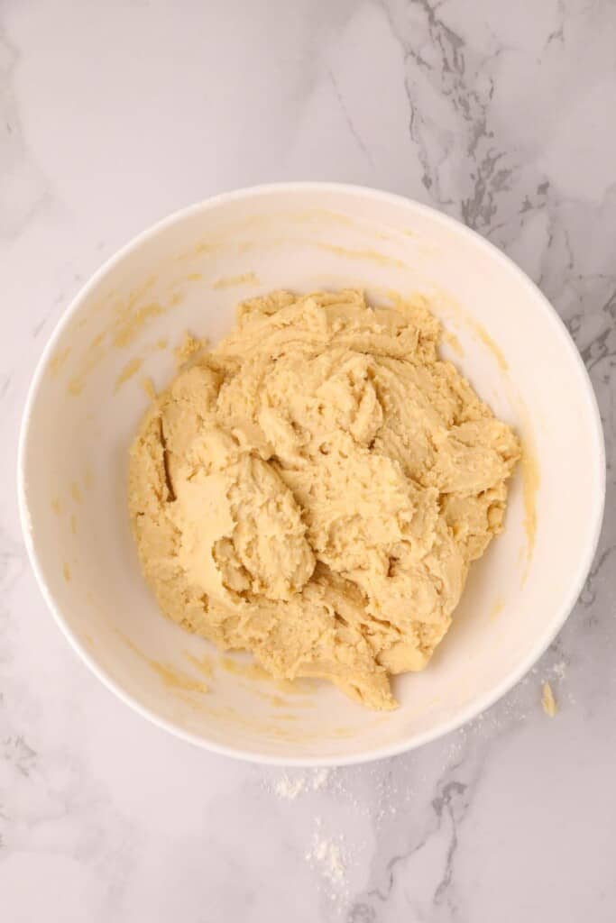 Combining ingredients for sugar cookie dough in a white mixing bowl.