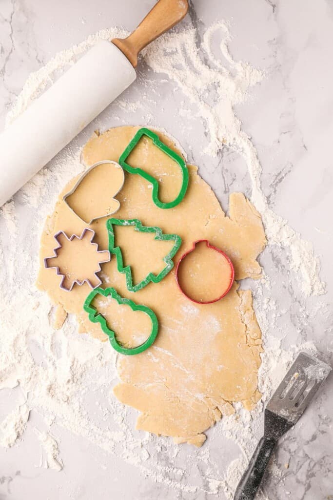 Chilled cookie dough rolled out on a floured surface. Cookie cutters on top to cut out shapes.
