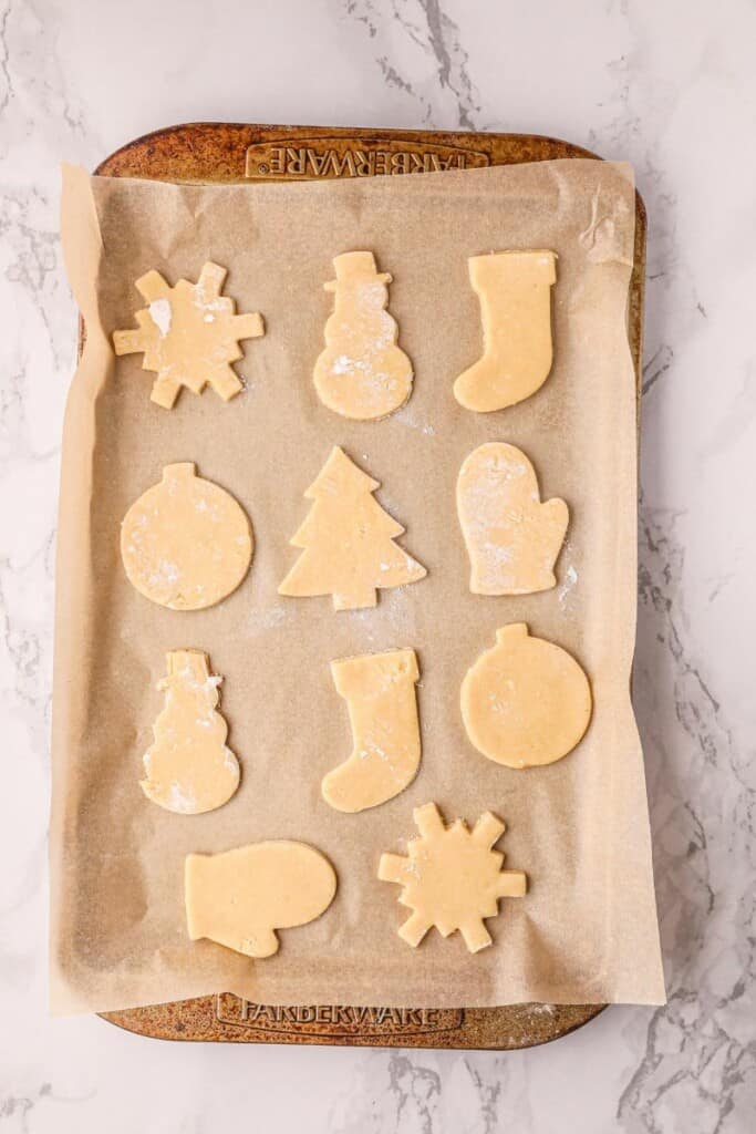 Twelve sugar cookie dough cut outs on a parchment lined baking sheet.