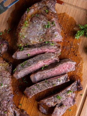 A New York Strip Steak cut into slices on a wooden cutting board.
