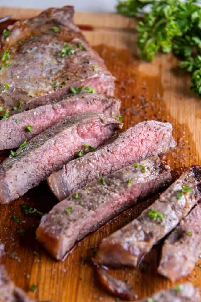 Close up view of slices of new york strip steak on a wooden cutting board.