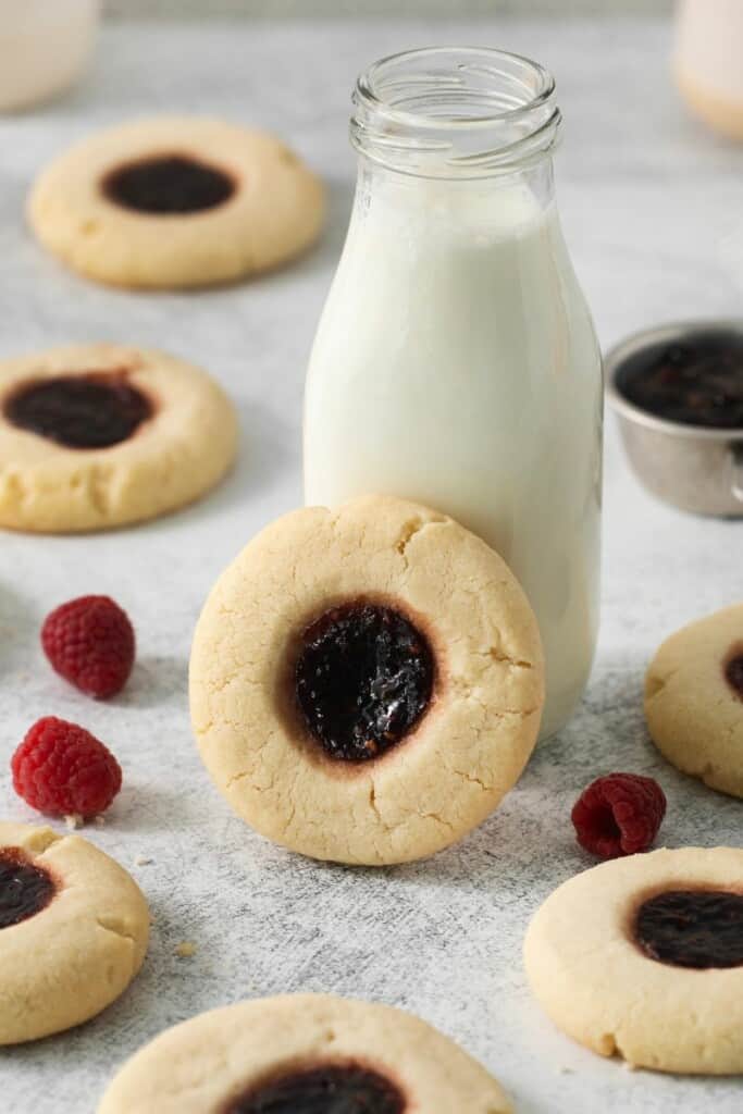 A raspberry thumbprint cookie lying against a small jug of milk.