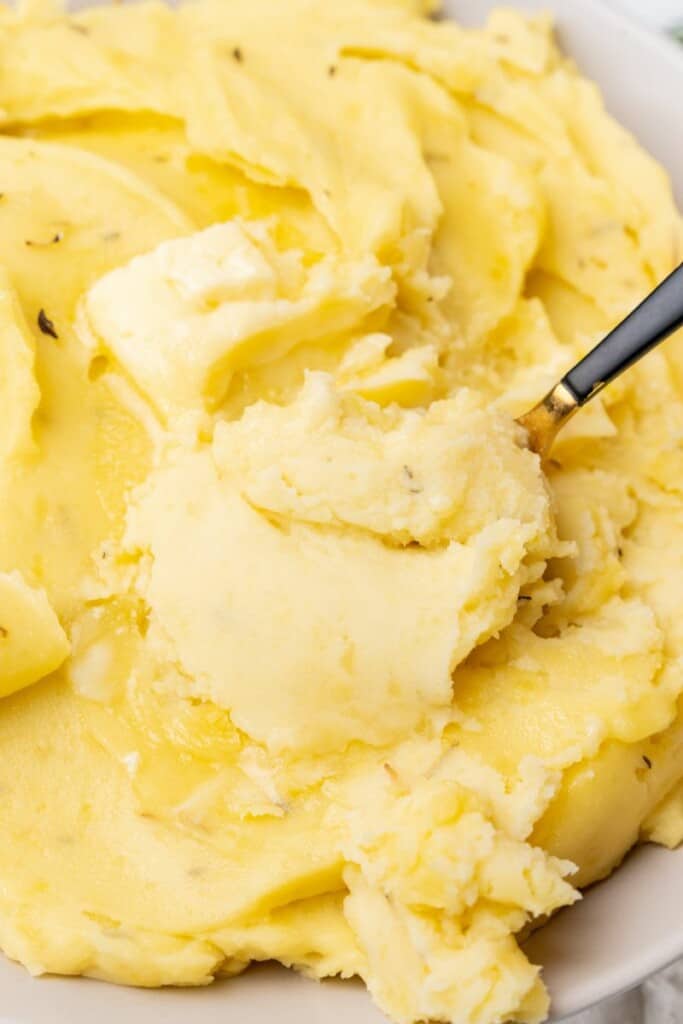 A close up view of a spoon lifting a bite of mashed potatoes from a serving bowl.