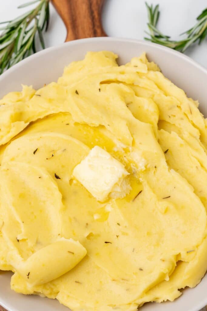 A close up view of a serving bowl of mashed potatoes topped with butter.