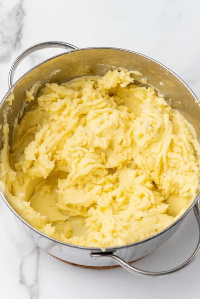 Adding buttery cream seasoning to potatoes in stockpot, then mashing them.