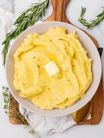 A serving bowl of rosemary seasoned mashed potatoes topped with butter.