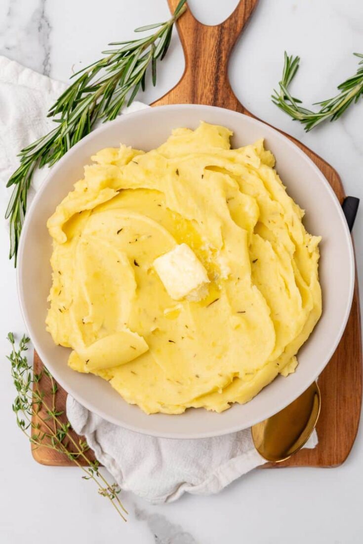 A serving bowl of rosemary seasoned mashed potatoes topped with butter.