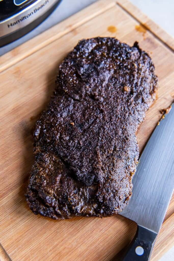Slow cooked skirt steak resting on a wooden cutting board with a chef's knife.