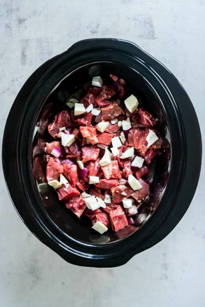 Steak cubes with all the seasonings and spices in a black crock pot.