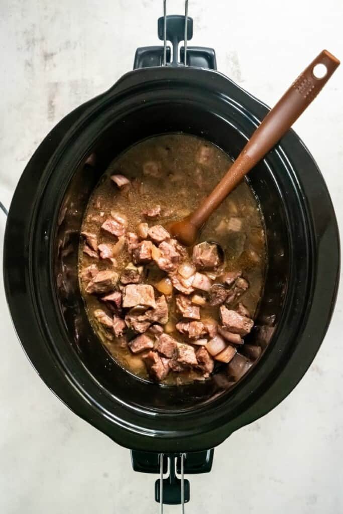 Seasoned steak cubes after cooking in a black crock pot.