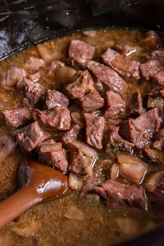 Close up view of prepared steak cubes in a black crock pot.