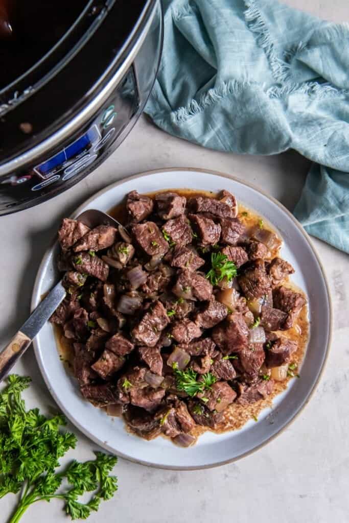 A serving of crock pot steak cubes on a plate next to a blue napkin.