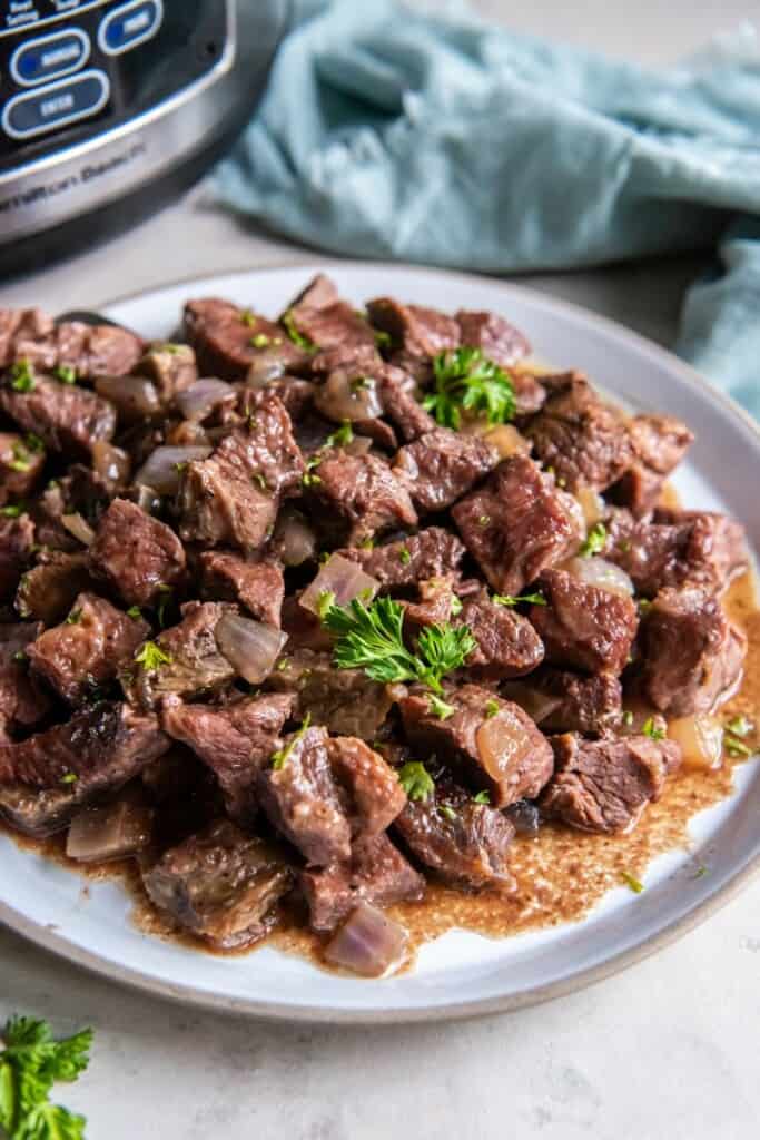 Steak Cubes prepared in a crock pot on a plate next to a blue napkin.