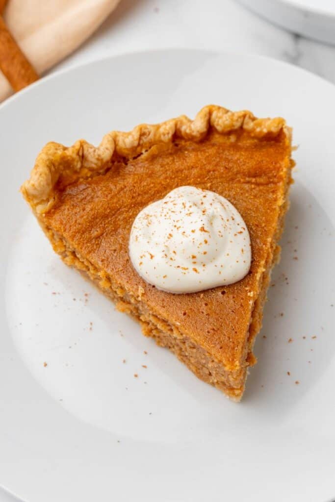 A slice of sweet potato pie topped with whipped cream on a white plate.