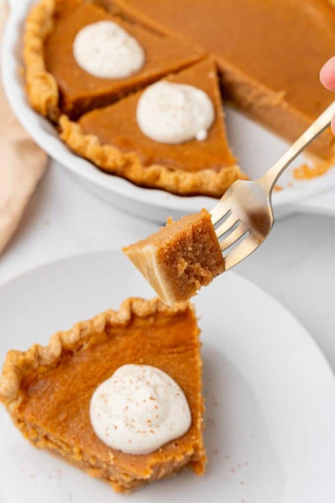 A fork holding a bite of sweet potato pie over a full slice on a plate.