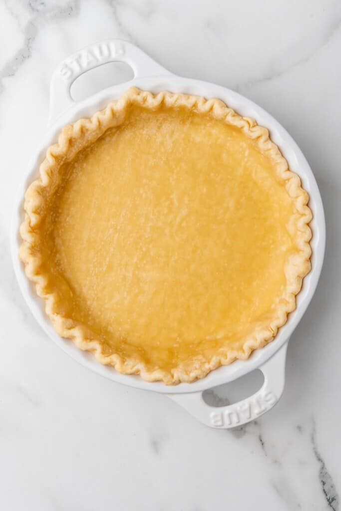 Partially baked pie crust in a white pie dish.