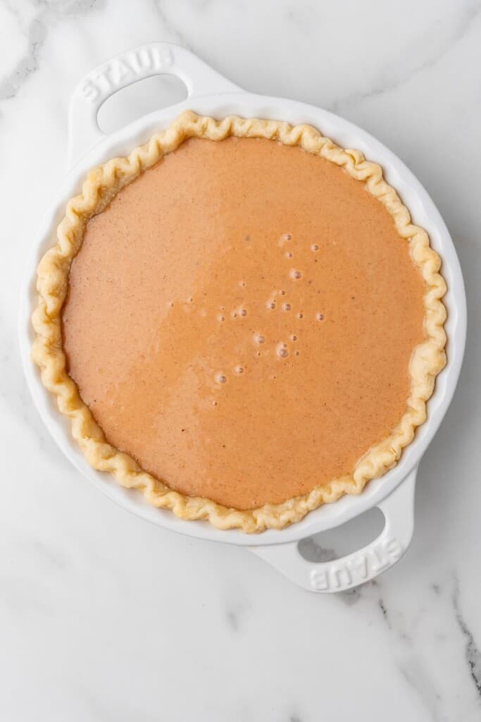 Pie filling in pie crust in a white pie baking dish.