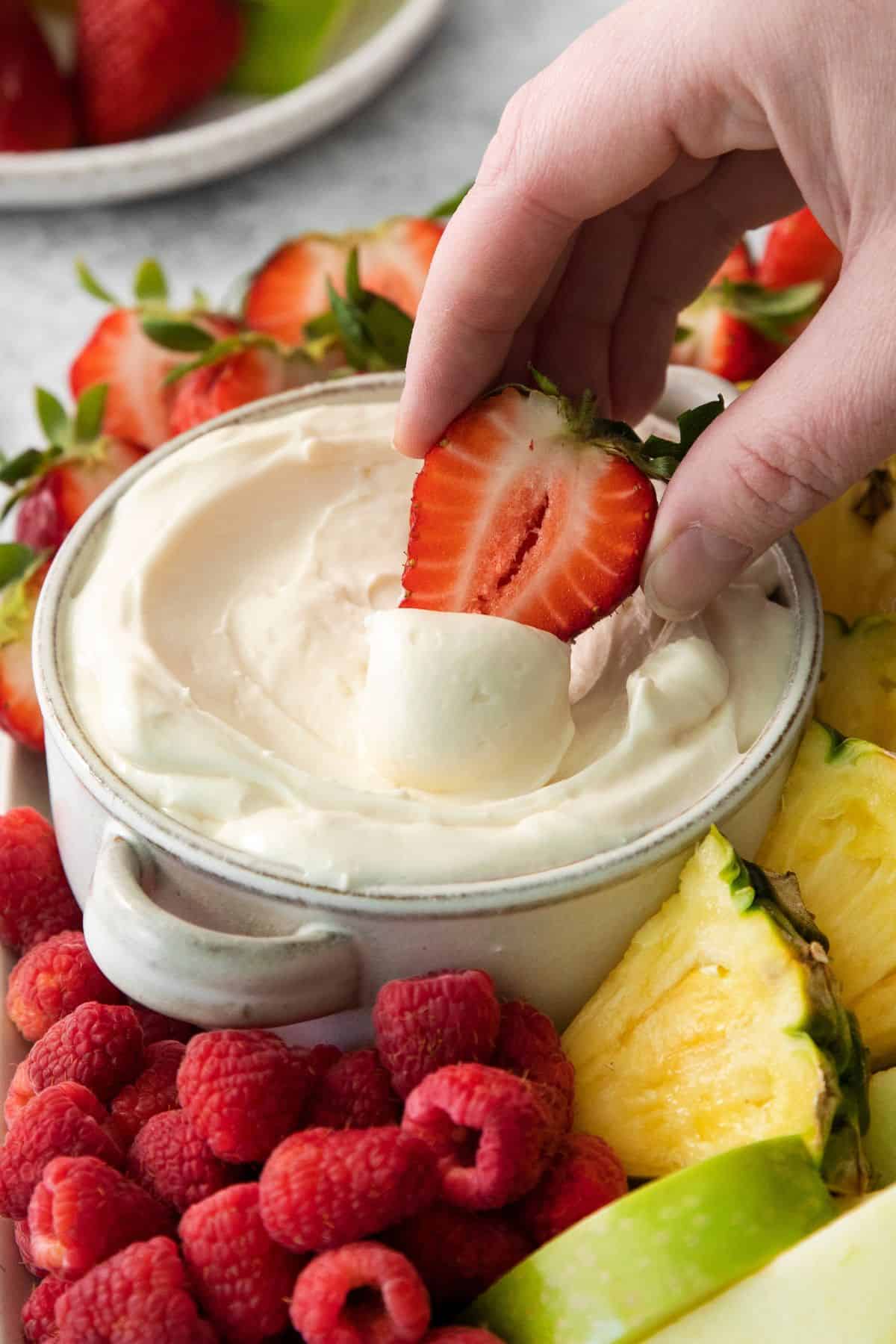 Dipping a strawberry into the marshmallow fruit dip to show the texture of how the dip looks when being scooped up.