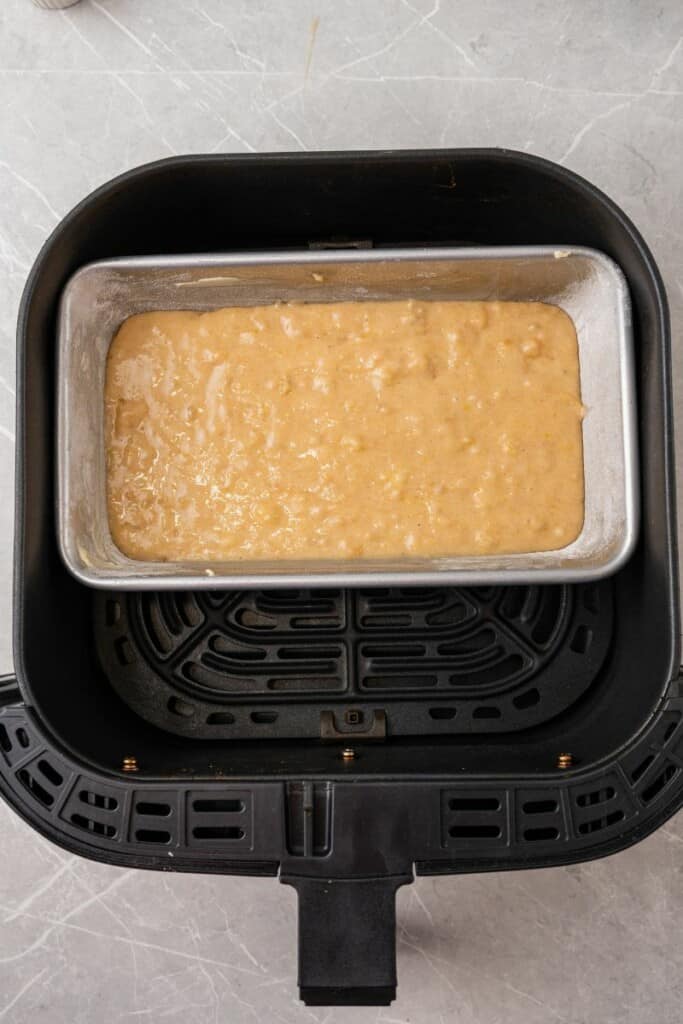 Banana Bread batter in a loaf baking pan inside a black air fryer basket.