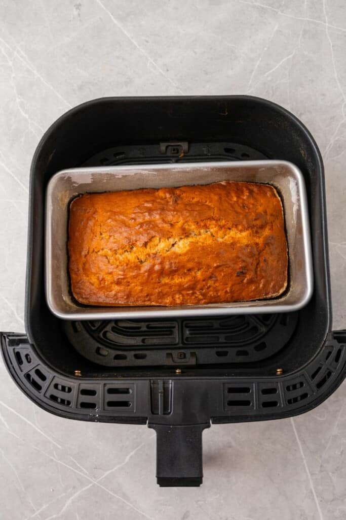 Baked banana bread in a loaf pan inside of a black air fryer basket.