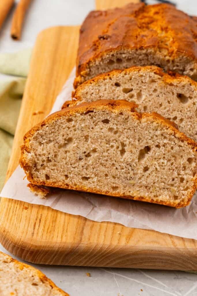 A loaf of banana bread cut into slices on a parchment lined wooden cutting board.