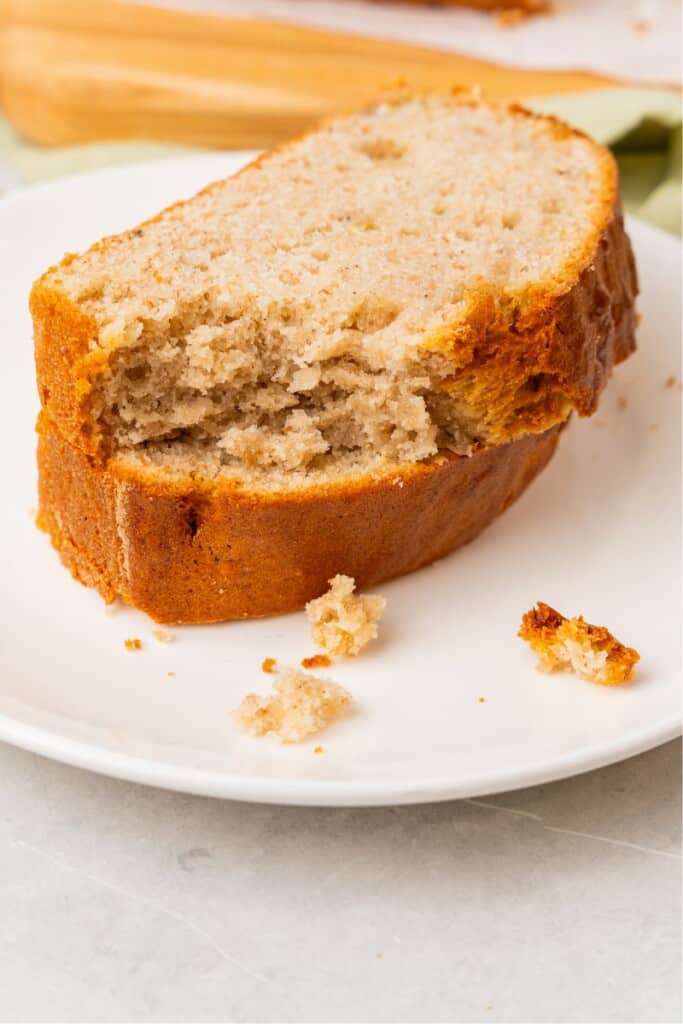 A closeup view of 2 slices of banana bread on a saucer, the top slice has a bite removed.