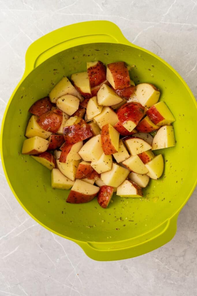 Cut potatoes in a mixing bowl with seasonings and spices.