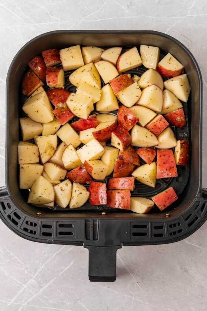 Seasoned red potatoes lying in a single layer of a black air fryer basket.