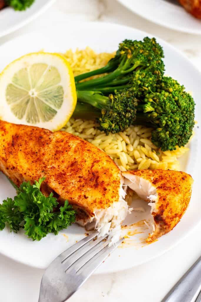 Air fry halibut on a white plate cut in half to see the flakiness.