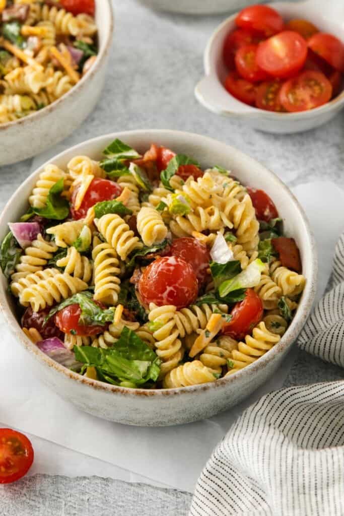 A bowl of pasta salad with tomatoes in the background.