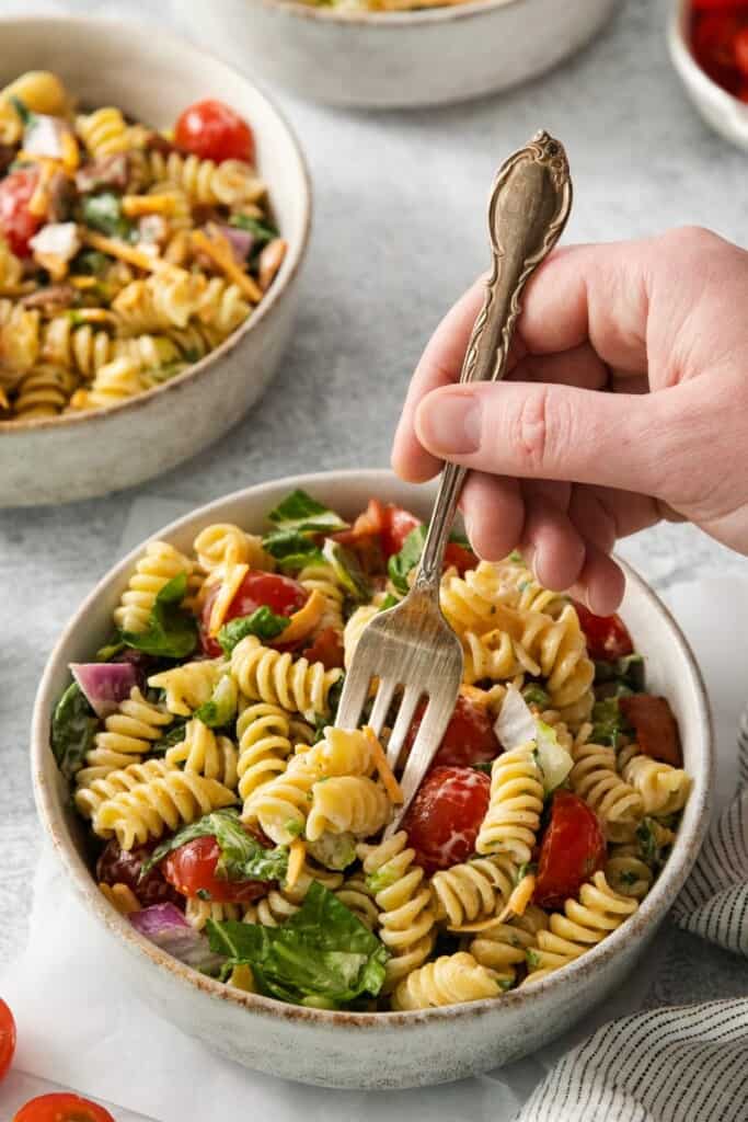 A fork lifting a bite of BLT Pasta Salad from a bowl.