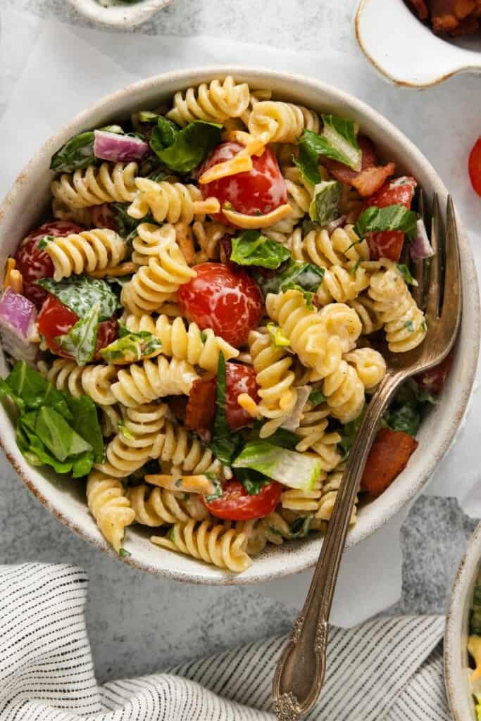 A closeup view of a bowl of BLT Pasta Salad with a fork resting in the bowl.