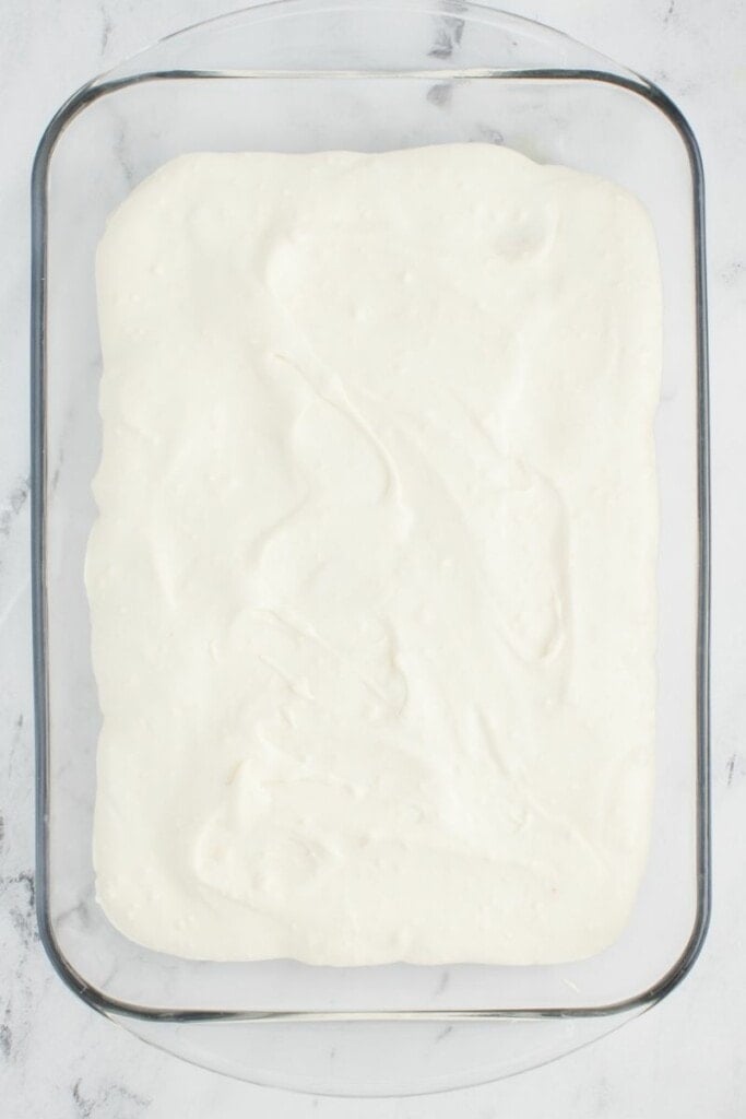 pouring more whipped pudding over banana pudding.