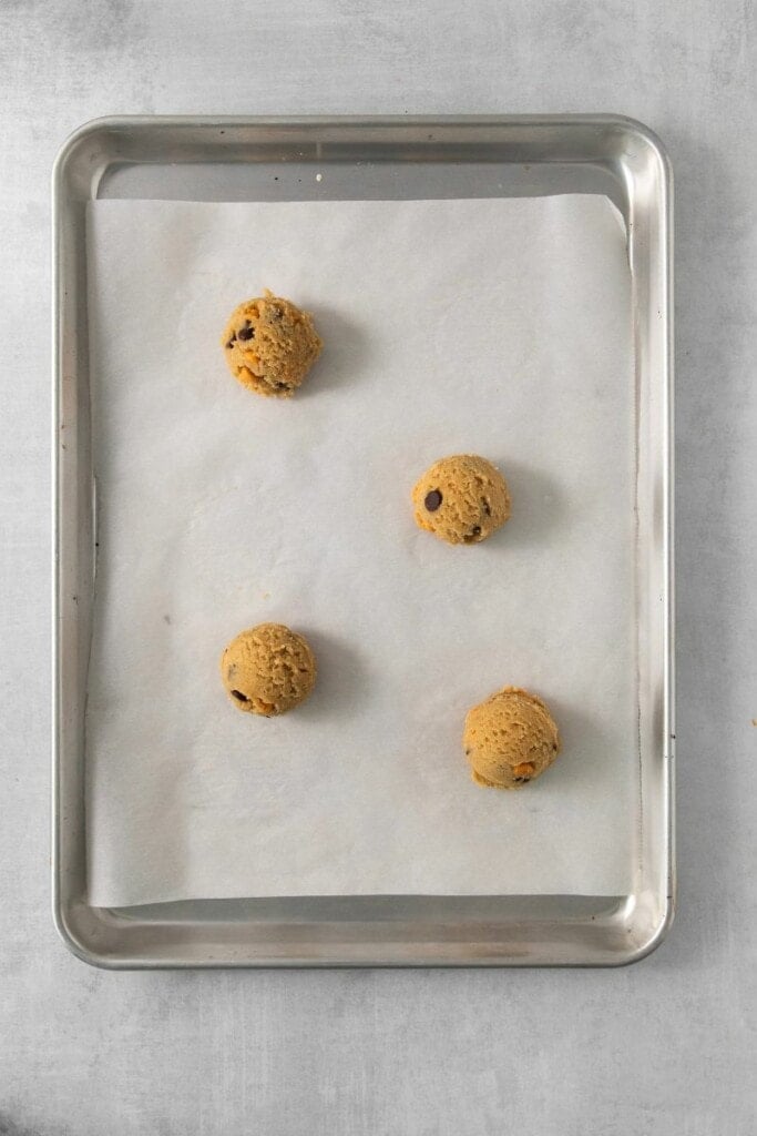 Four cookie dough balls on a parchment lined baking sheet.