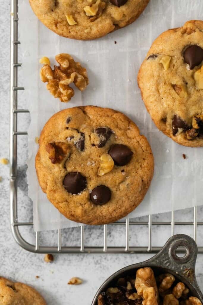 Close up view of a baked walnut chocolate chip cookie on a parchment lined cooling rack.